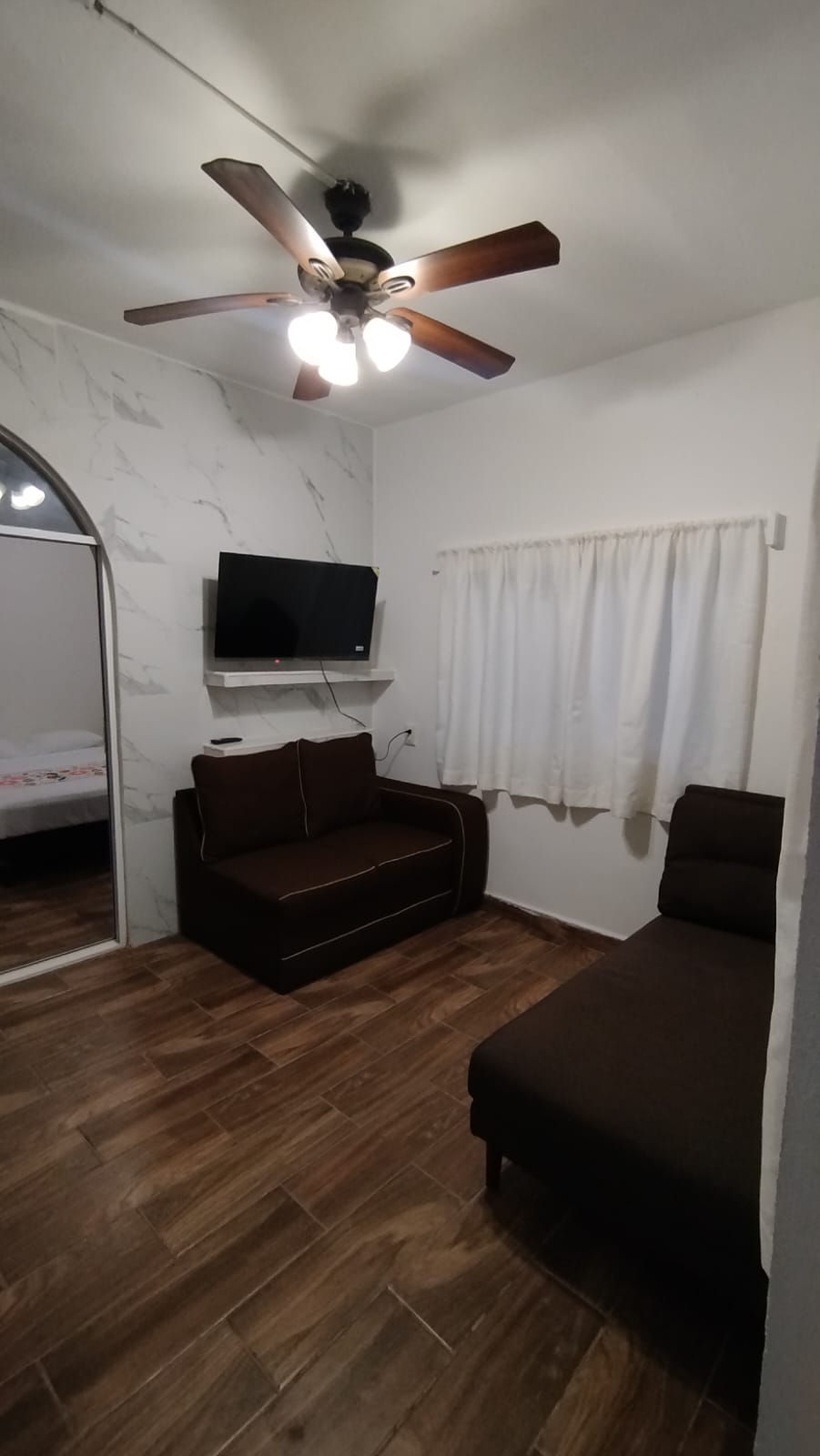 Vista de la sala, sillones, televisi&oacute;n y ventilador de techo.